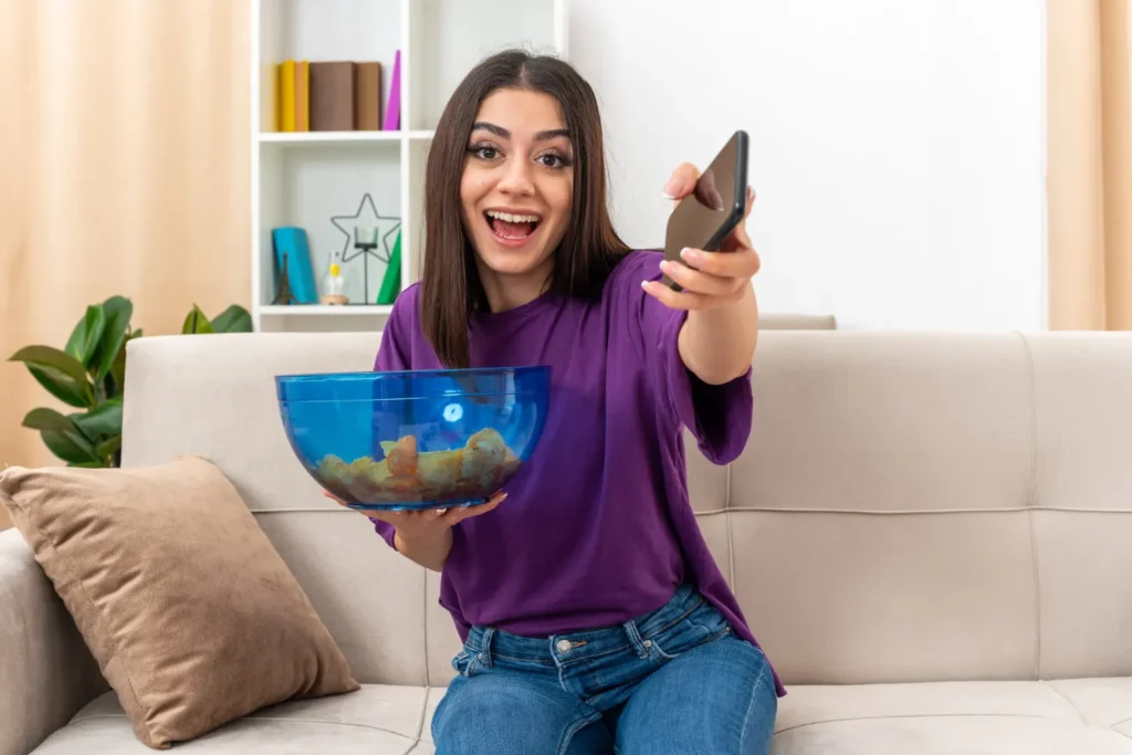 Femme enthousiasmée regardant du contenu IPTV sur son smartphone tout en profitant du streaming de télévision française à la maison